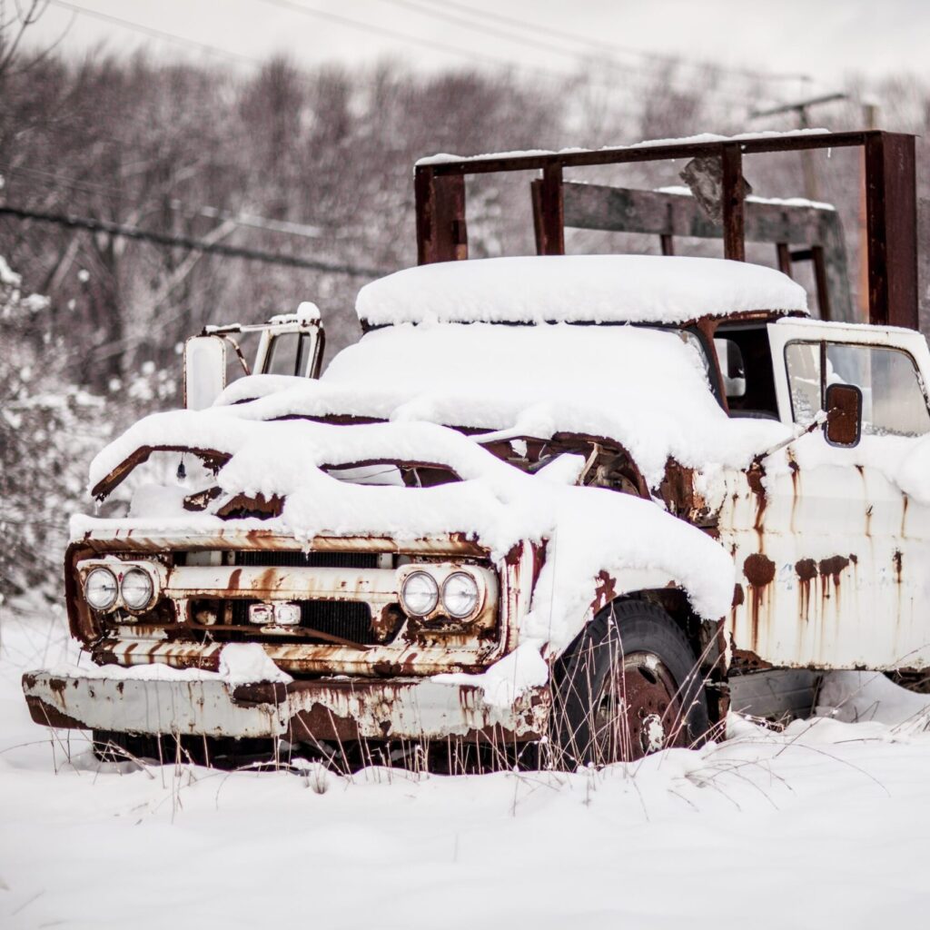 Landscape picture of a late 60 pickup truck abandoned and rusted parked in the snow.