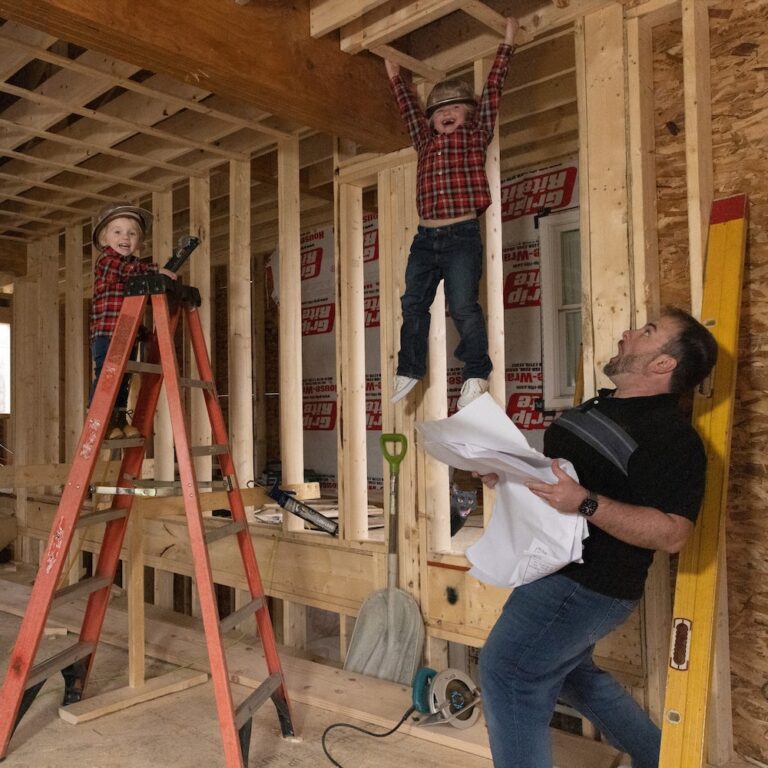 The Carroll family working in construction. One boy is on a ladder, one boy is hanging from the ceiling, the father is shocked.