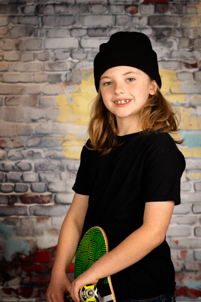 Young boy holding a skateboard while smiling.