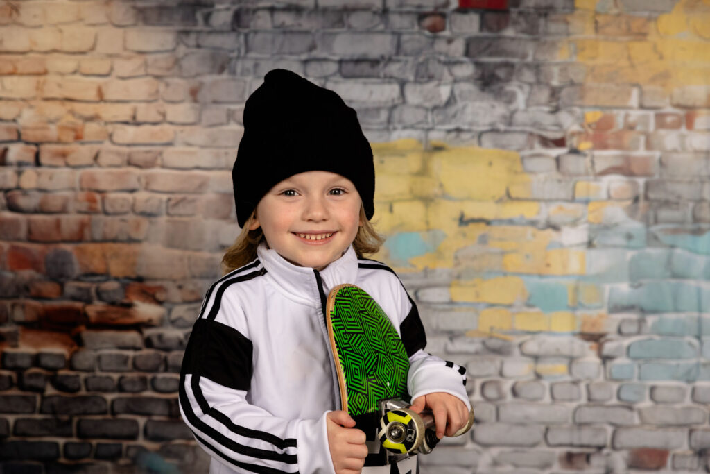 A young boy holding a skateboard wearing a hat.