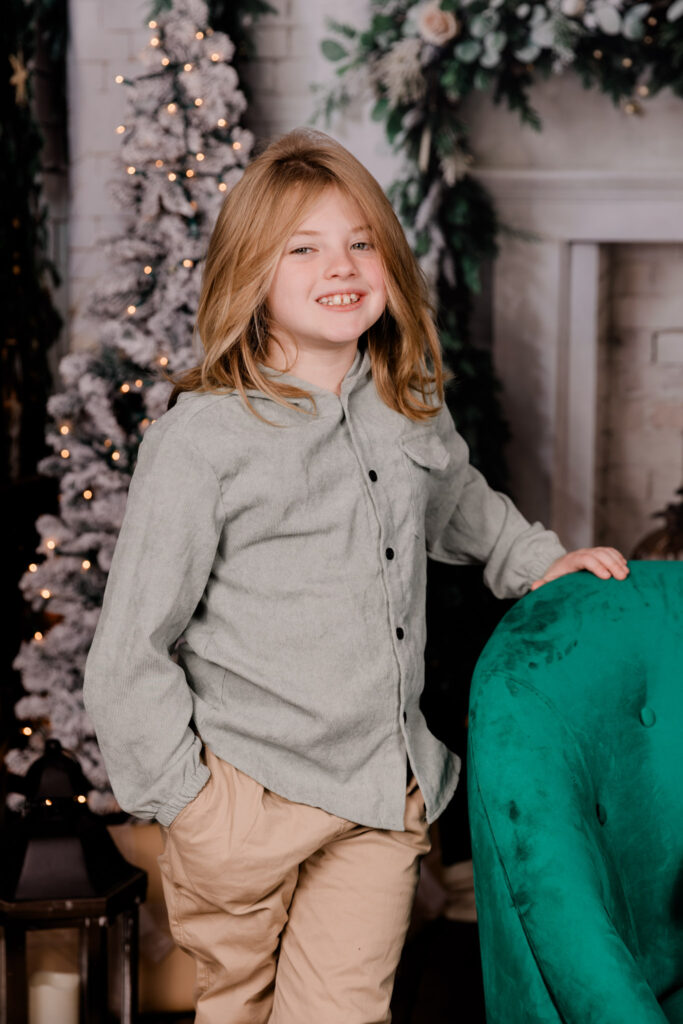 A young boy standing next to a green chair.