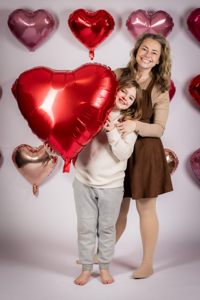 Mom and young son holding a heart balloon and smiling.