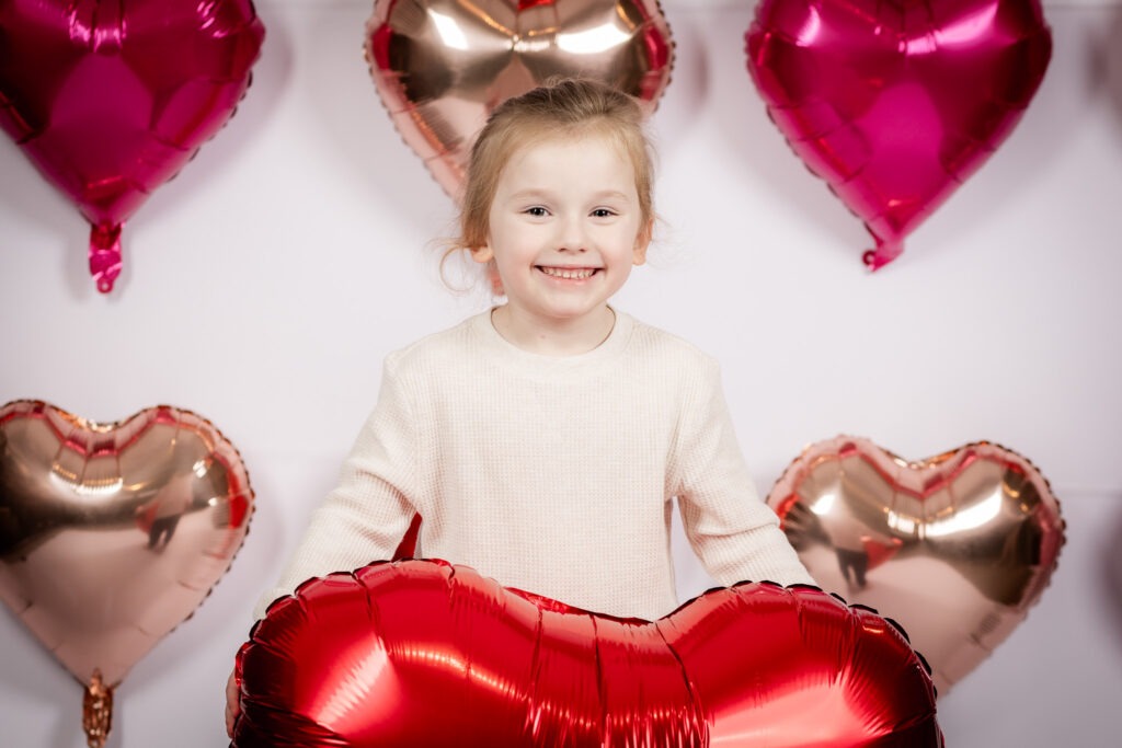 A young boy smiling and holding a heart balloon.