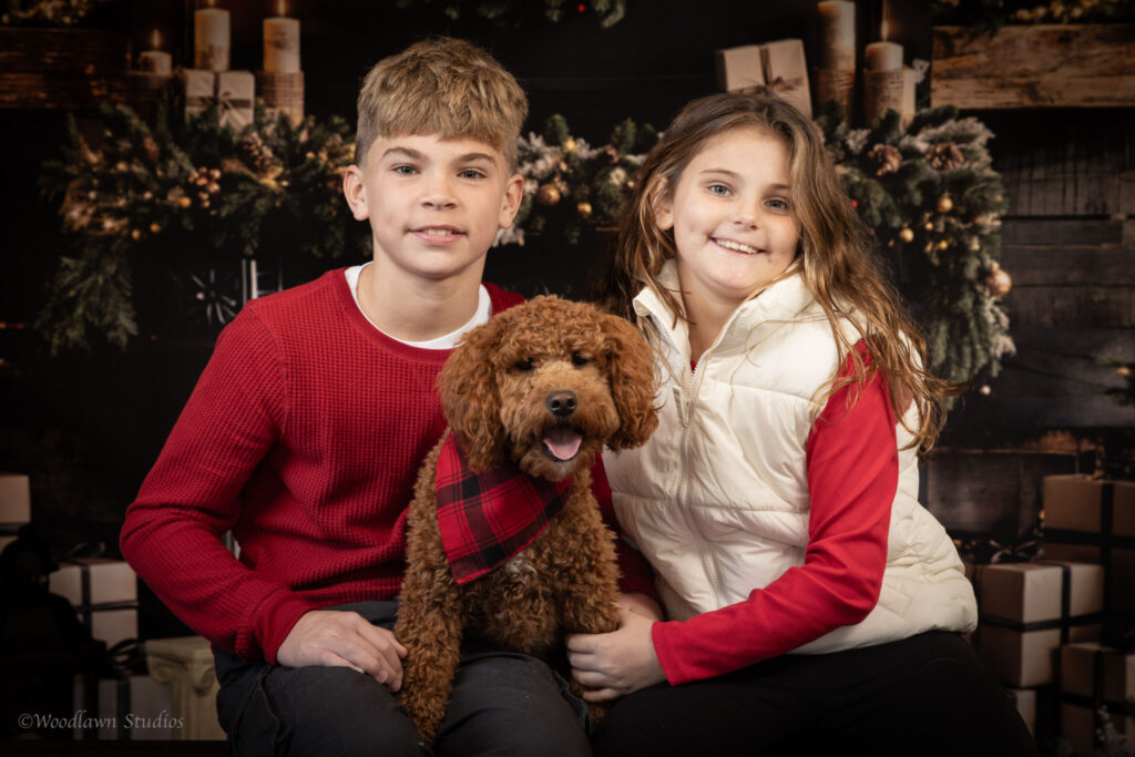 Brother, sister, and pup smiling for holiday portraits.